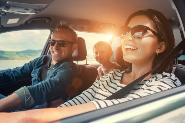 A family driving in a car smiling with sunshine shining in.