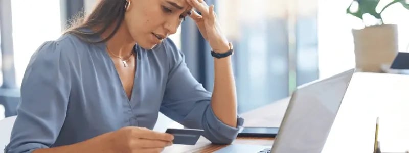 A woman looks stressed whilst sat at a desk looking at a credit card.