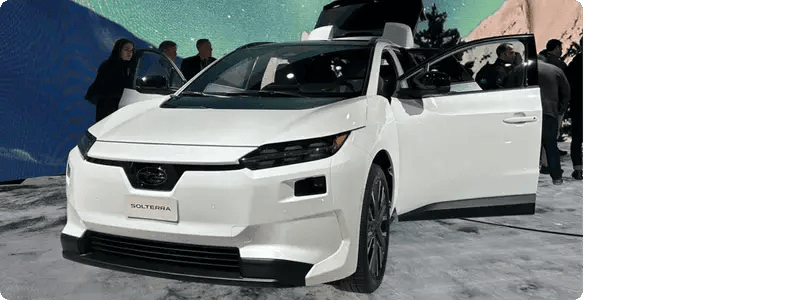 The white Subaru Solterra in a showroom setting with its doors open and people inspecting the car.