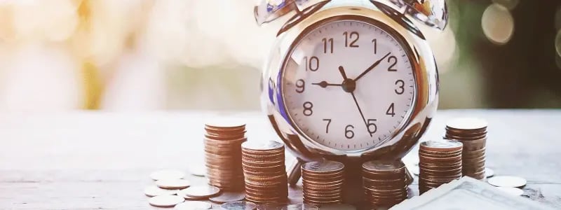 An alarm clock on top of stacks of coins, representing the value of money over time.