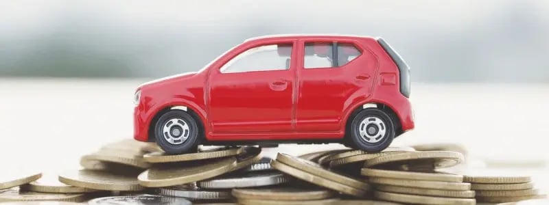 A red toy car placed side on, on top of a mound of coins, representing car finance.