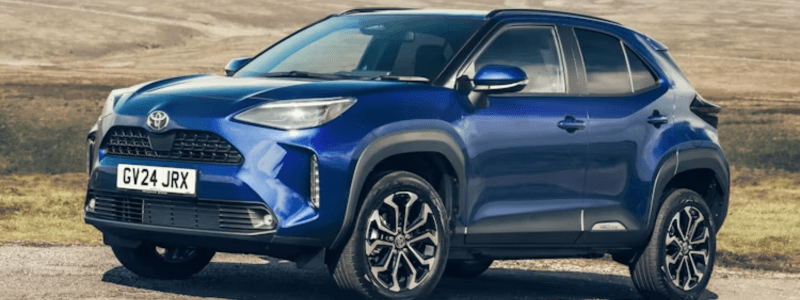 A blue Toyota Yaris Cross parked in front of a country landscape.