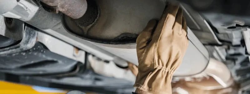 A person working on a catalytic converter under a car.