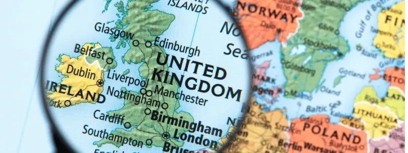 A magnifying glass focusing on the United Kingdom on a map, with major cities pinpointed.