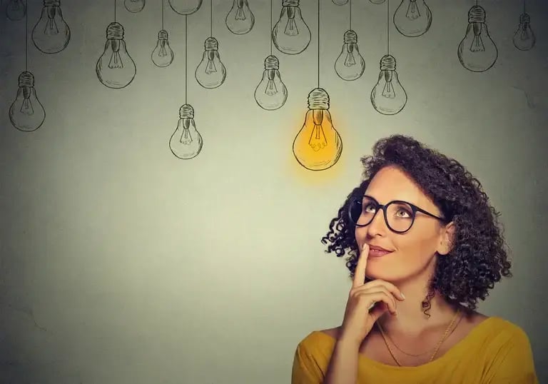 Thinking woman in glasses looking up with light idea bulb above head isolated on grey wall background