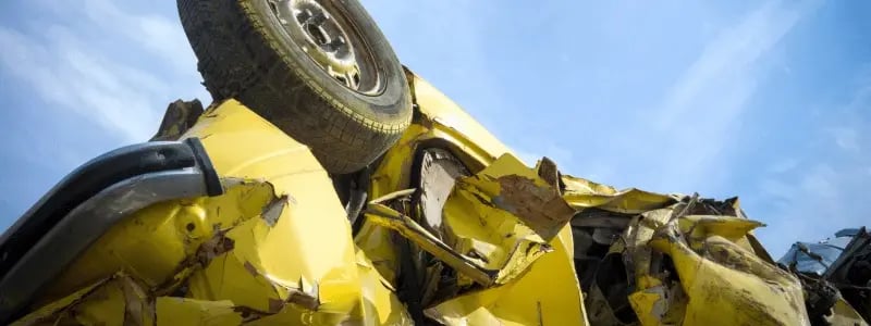 A close up of a damaged yellow car upside down, with a blue sky in the background.