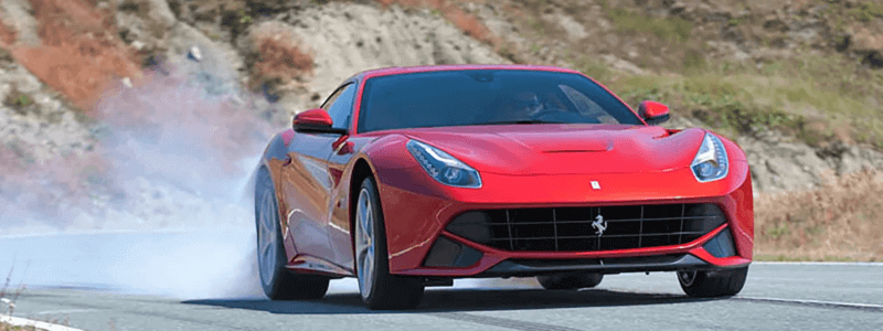 A red Ferrari driving quickly with a back tyre burning out.