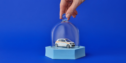 A hand placing a glass dome over a toy car, indicating protection and car insurance.