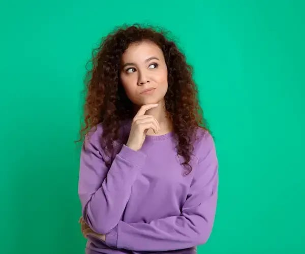 A woman stood in thought against a teal/green background.