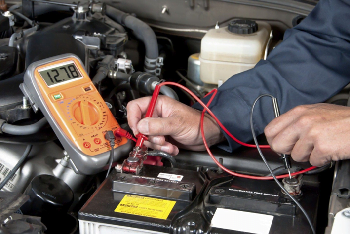 Car mechanic checks the battery of a car with the bonnet up.