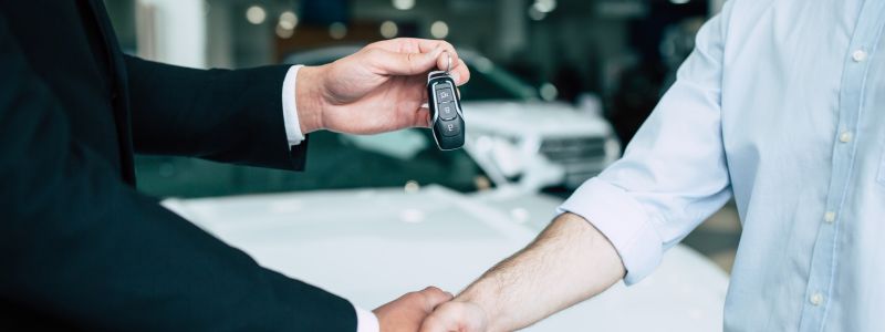 Two people shake hands and exchange car keys in a car showroom.