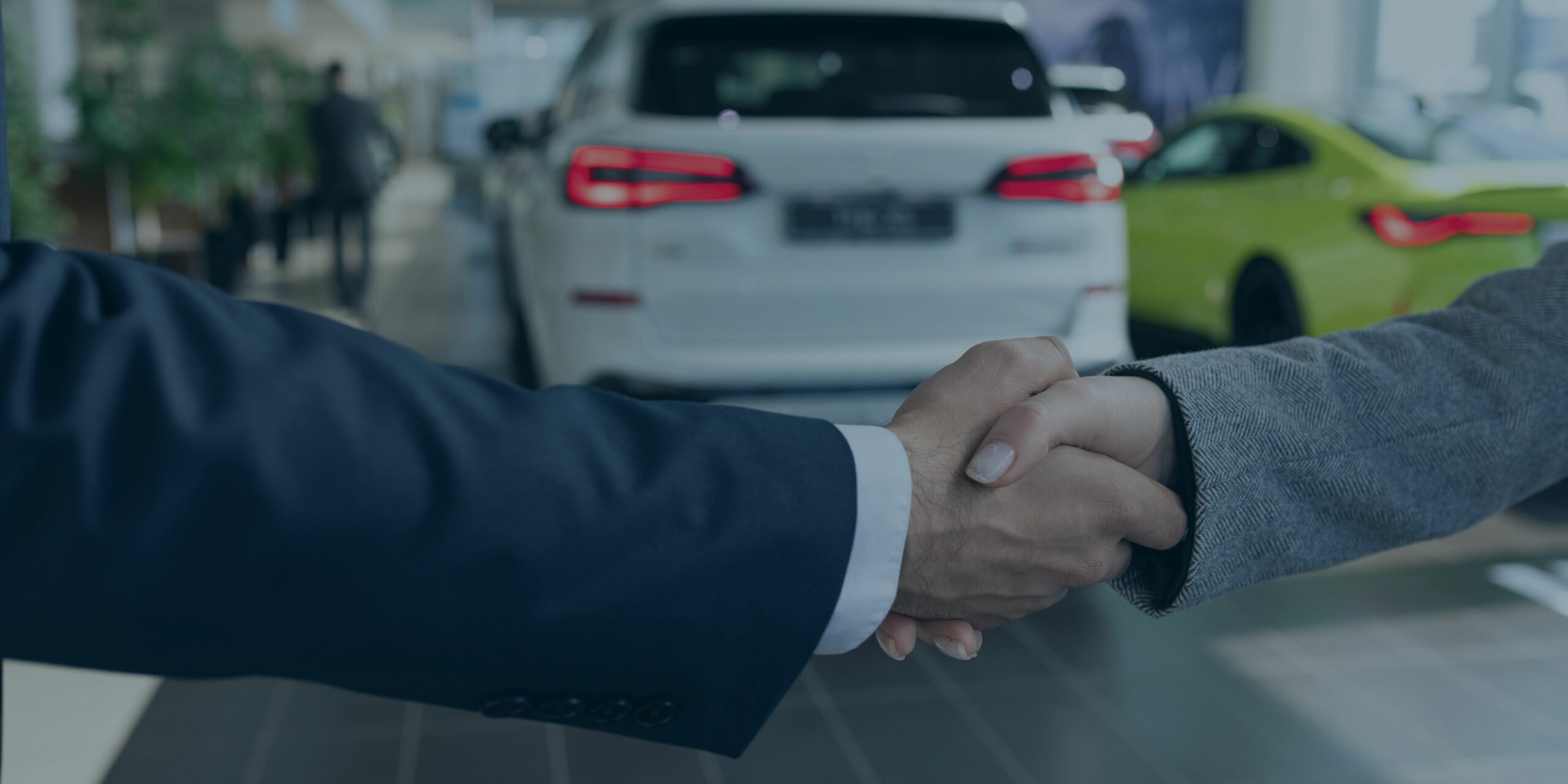 Two people shaking hands at a car dealership.