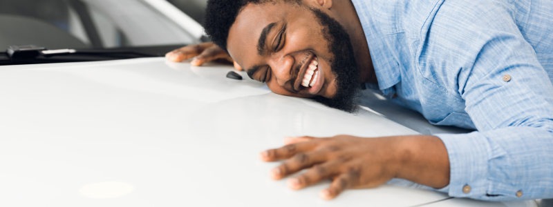 A person hugging the bonnet of a car whilst smiling.