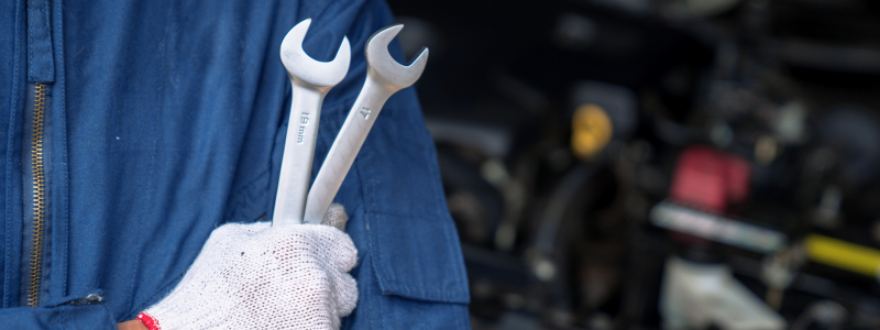 A close up of a mechanic holding two wrenches.