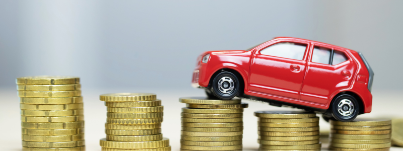 A red toy car positioned on coins ascending in amount from right to left.
