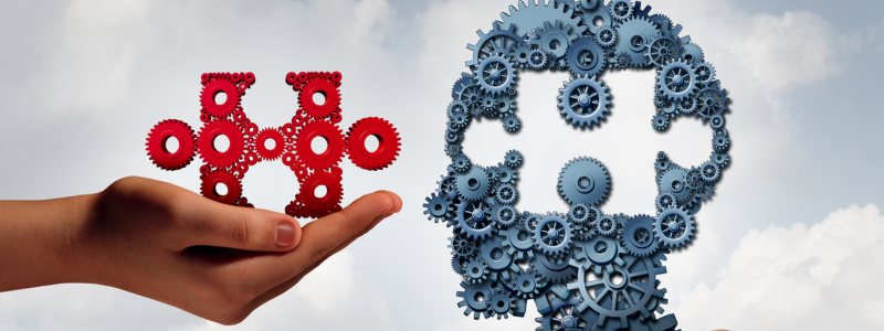 A hand holding red gears forming a jigsaw piece, with a background of a head silhouette made of blue gears against a cloudy sky, symbolizing the concept of financial intelligence or economic thinking.