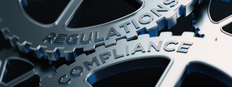 Interlocking gears with the words "REGULATIONS" and "COMPLIANCE" engraved on them, symbolising the interconnected nature of regulatory processes and compliance mechanisms.