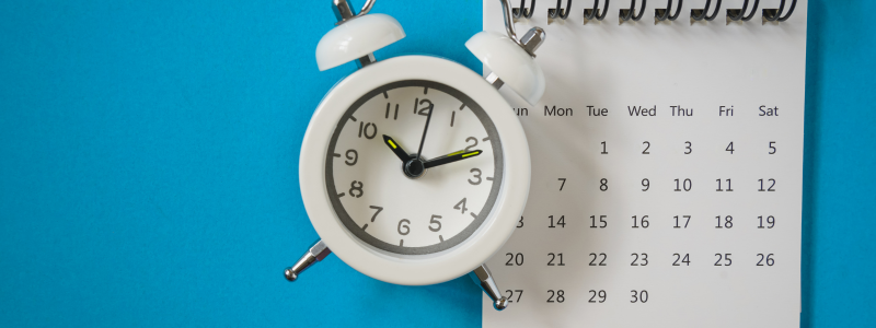 A small alarm clock next to a calendar on a blue background.